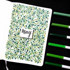 an open notebook with the word may written on it next to green pens and markers