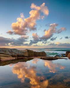 the reflection of clouds in the water is seen at sunset on the rocks near the ocean