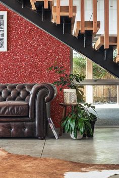 a brown leather couch sitting under a stair case next to a wooden banister and potted plant