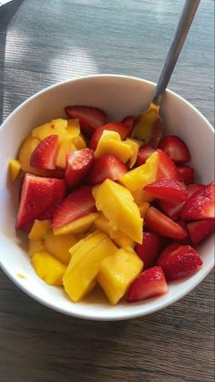 a white bowl filled with cut up fruit on top of a wooden table next to a fork