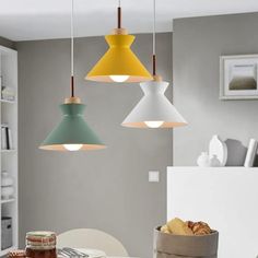 three different colored lights hanging over a table in a room with gray walls and white chairs