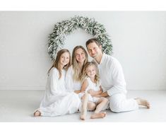 a family sitting in front of a white wall with a wreath on the wall behind them