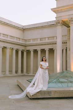 a woman standing in front of a building wearing a white dress and veil with her arms crossed