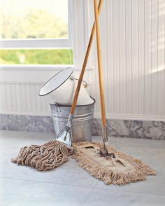 two mop heads and bucket on the floor in front of a window with white walls