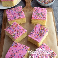 several pieces of cake with pink frosting and sprinkles on a cutting board