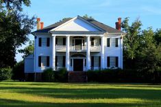 a large white house sitting in the middle of a lush green field next to trees