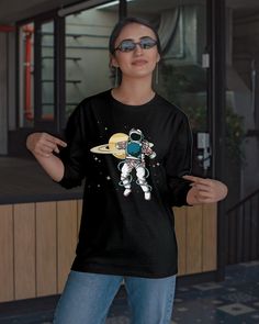 a woman wearing sunglasses and an astronaut t - shirt is standing in front of a building