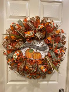 an orange and brown wreath on the front door with pumpkins, leaves and burlocks