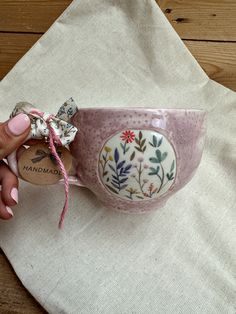 a hand holding a pink cup with floral designs on it and a tag attached to the handle