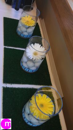 three clear vases filled with water and yellow flowers on top of a green mat