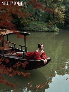 a woman in a red dress is sitting on a boat that is floating down the river