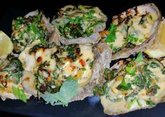 several pieces of bread with cheese and greens on it sitting on a black plate next to some lemon wedges