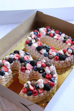 two cakes in a box decorated with berries, strawberries and other fruit toppings