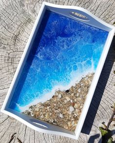 an empty tray sitting on top of a tree stump next to the ocean and sand