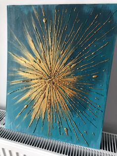 an abstract painting with gold and blue colors on a white wall next to a radiator