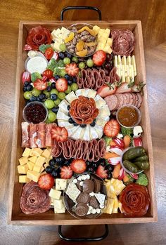 a wooden tray filled with lots of different types of cheese and meats on top of a table