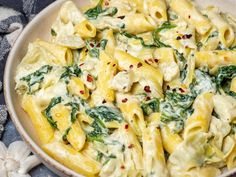 a white bowl filled with pasta and spinach covered in sauce on top of a table