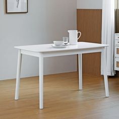 a white table with two cups on it in front of a painting and dressers