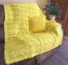 a yellow crocheted blanket sitting on top of a couch next to a potted plant