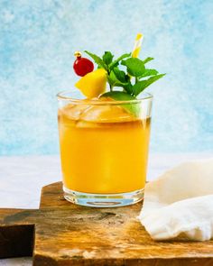 a glass filled with orange juice and garnish on top of a wooden cutting board