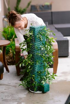 a woman bending over to look at a green plant in a potted planter