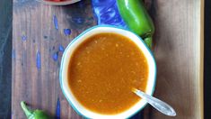 there is a bowl of soup on the table next to two peppers and a spoon