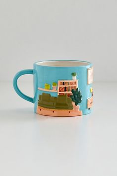 a blue coffee mug with an image of a house and trees on the front, sitting on a white surface