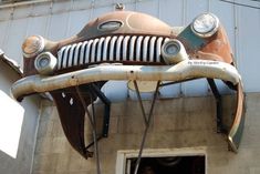 an old, rusty car is hanging from the side of a building with its hood up