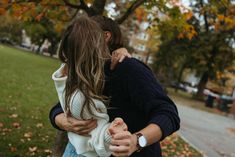 a man and woman embracing each other in the park on a fall day with leaves falling all over the ground