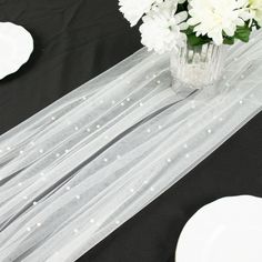 white flowers are in a vase on a black table cloth with plates and napkins