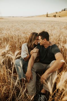 a man and woman sitting in the middle of a wheat field with their arms around each other