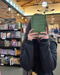 a woman holding up a book in front of her face with both hands and looking at it