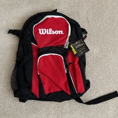 a red and black backpack sitting on top of a carpeted floor next to a tag