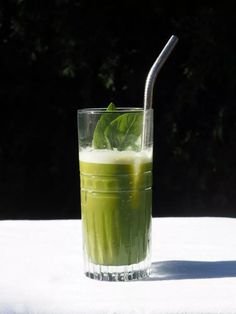 a glass filled with green liquid on top of a white table