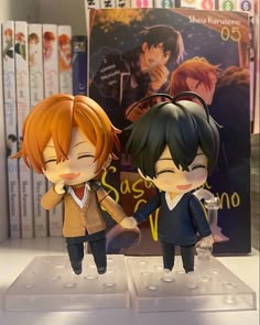 two anime figurines on display in front of books