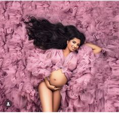 a pregnant woman laying on top of a bed of pink ruffles with her hair blowing in the wind