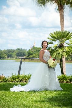 a woman in a wedding dress posing for a photo by the water with palm trees