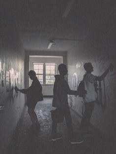 three people standing in an empty hallway with graffiti on the walls and one person holding a backpack