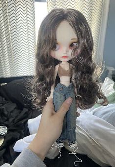 a doll is being held up by someone's hand in front of a bed