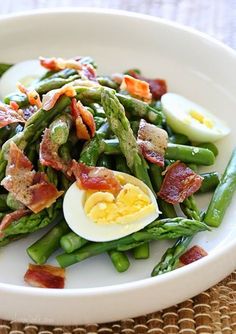 asparagus with bacon, hard boiled eggs and green beans on a white plate