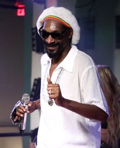 a man holding a wine glass and giving the peace sign with his right hand while standing on stage