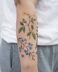 a woman's arm with blue flowers and green leaves on the left side of her arm