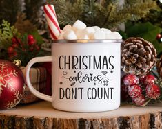 a christmas mug with marshmallows and candy cane in it sitting on a tree stump