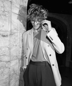 black and white photograph of a woman in glasses leaning against a wall with her hand on her head