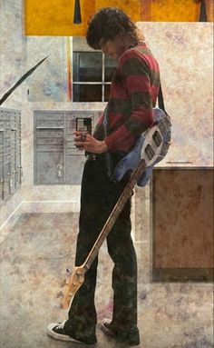 a man standing in a kitchen holding a guitar and looking at his cell phone,