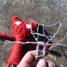 a hand is holding a red knitted toy with wires attached to it, on top of a rock