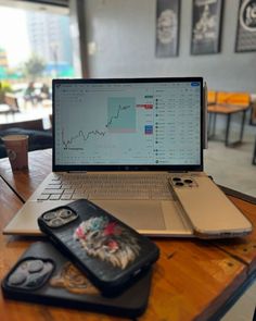 an open laptop computer sitting on top of a wooden table next to two cell phones