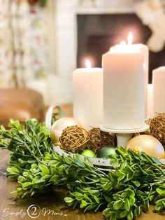 three candles sitting on top of a table next to christmas decorations and greenery in front of a fireplace