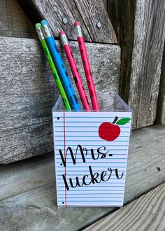 a cup that has some pencils in it and an apple on the side of it