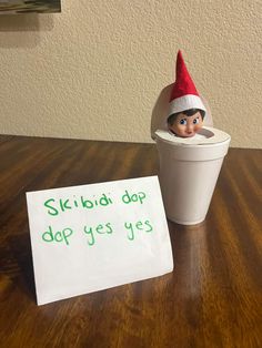 an elf's hat on top of a cup next to a sign that says skibia dap do yes yes